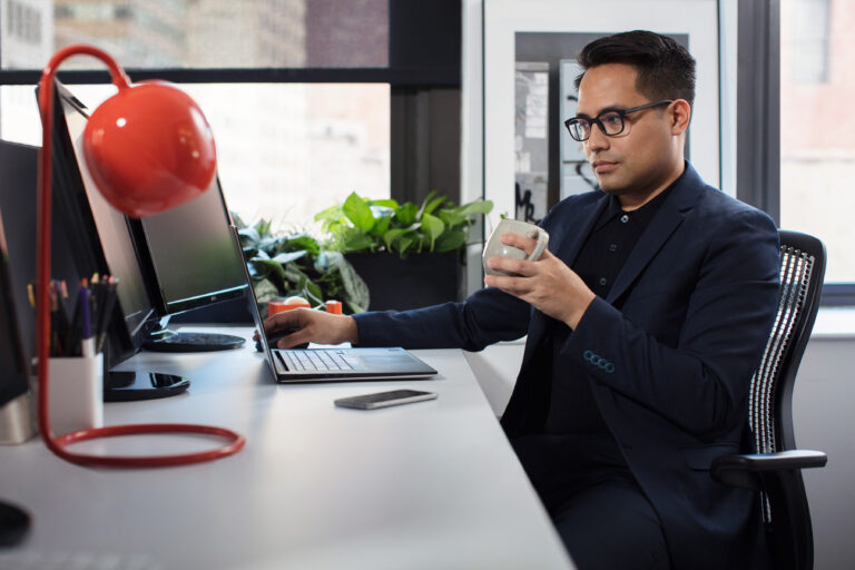 man in a suit holding a coffee mug clicking through laptop