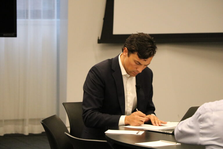 man in suit writing up documents at a table