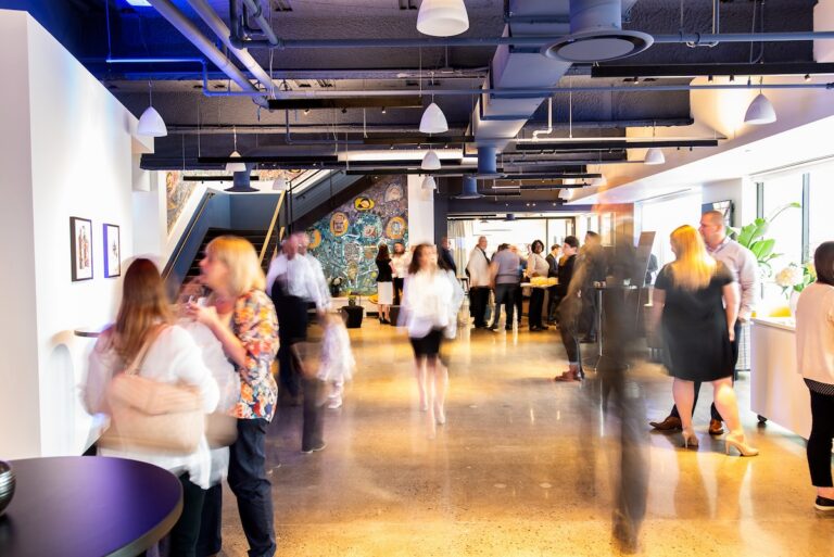 People mixing in a bright event space at Convene 30 S. 17th Street with an Isaiah Zagar mosaic artwork visible on the back wall.