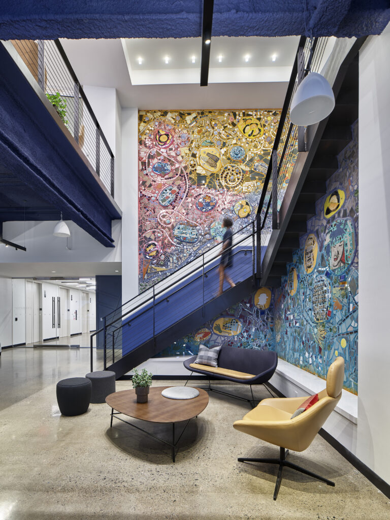 Persno walking down steps in Convene S. 30 17th Street with large mosaic by Isaiah Zagar covering the walls. 