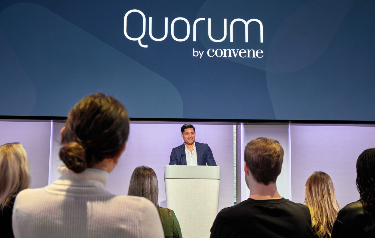A man stands in front of a podium as is presenting to a watching crowd of investors