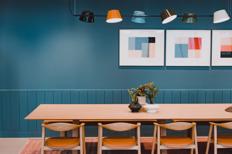 Photographed at Convene Willis Tower, a wooden table with six chairs is placed in front of a blue wall where there are three abstract art pieces on display.