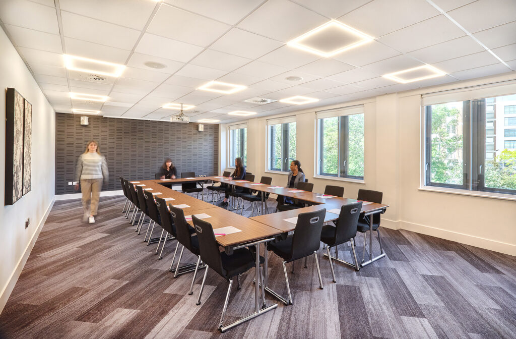 A table in the center of a boardroom with people surrounding it. 