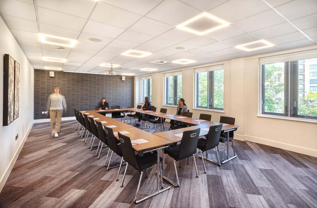 A table in the center of a boardroom with people surrounding it.