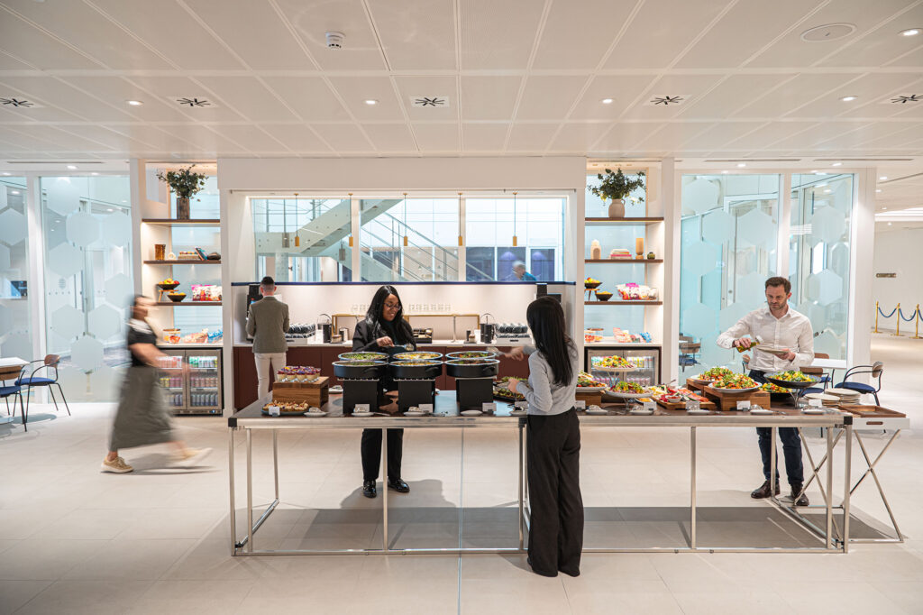 A group of delegates are taking food from a buffet scape that is at created in the gallery space at 133 Houndsditch, Liverpool Street