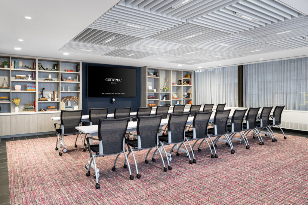 The Library, a meeting and event space at Convene One Boston Place, is set up in a classroom style with chairs and tables in long rows facing a screen. 