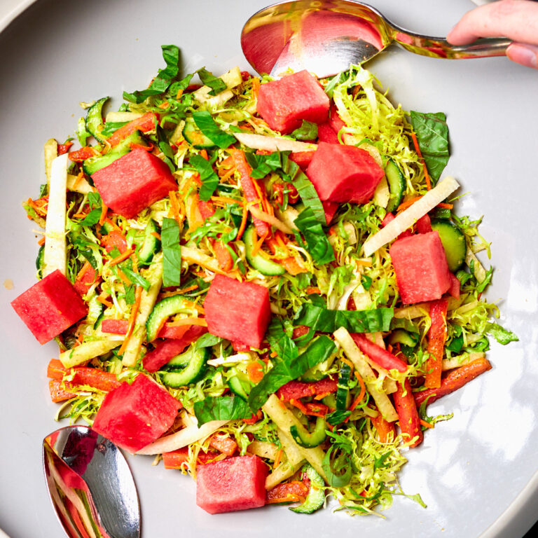 A close up shot of a Haloumi and Watermelon salad in a grey bowl. There are two large serving spoons.