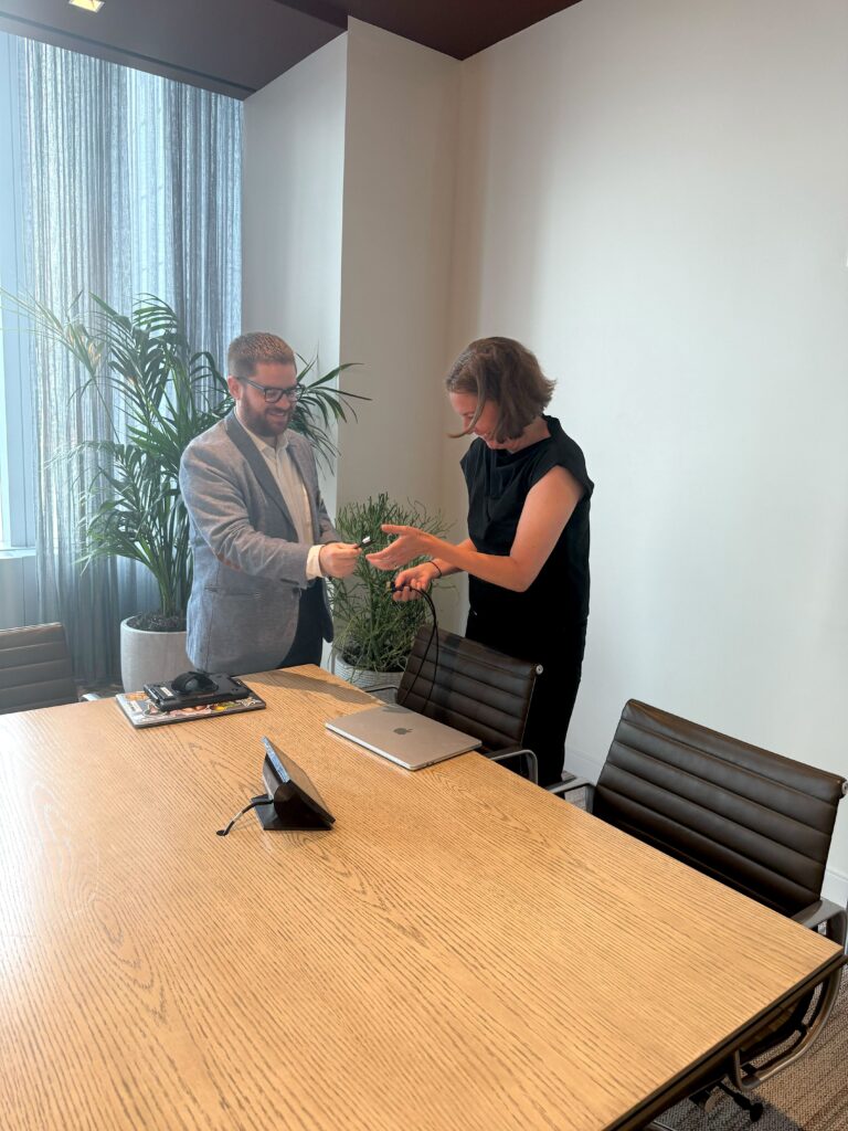 Convene AV Supervisor hands laughing woman a cord at a boardroom desk.