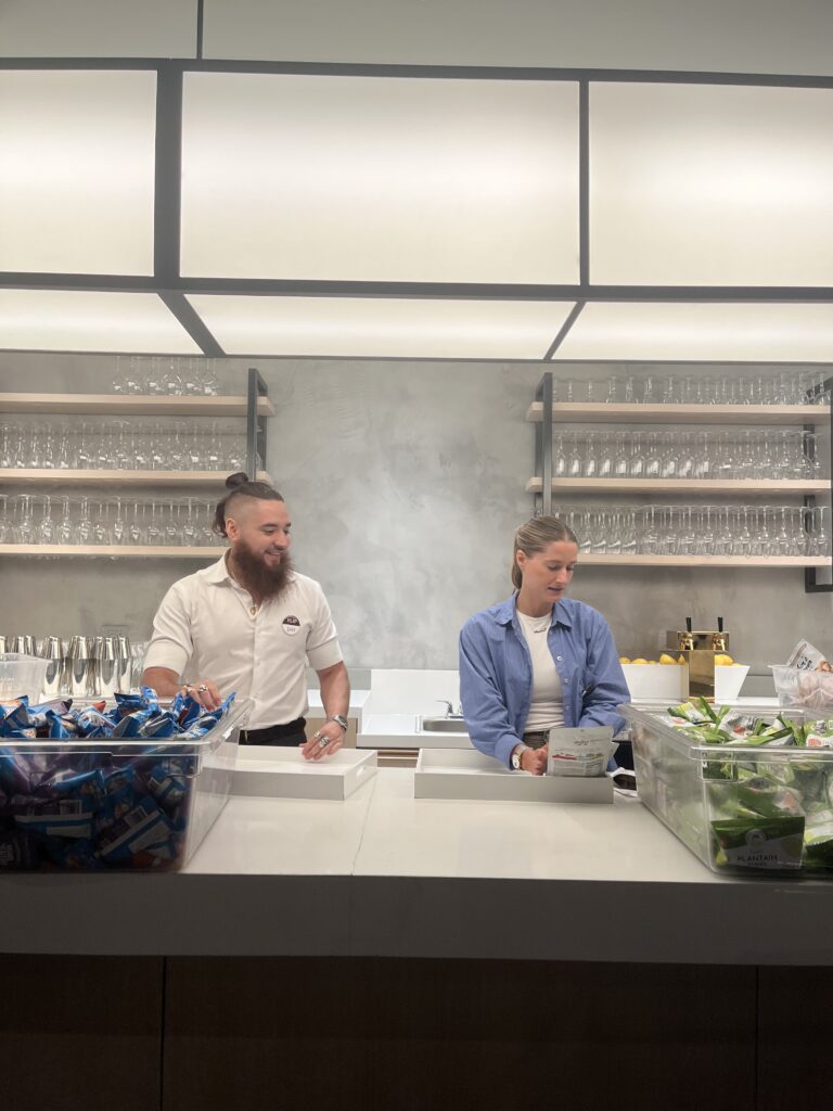 Two Convene staff gather snacks in bar area with glasses.