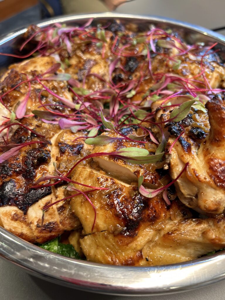 Yuzu-glazed chicken in chafing dish with purple garnish by Convene chefs.