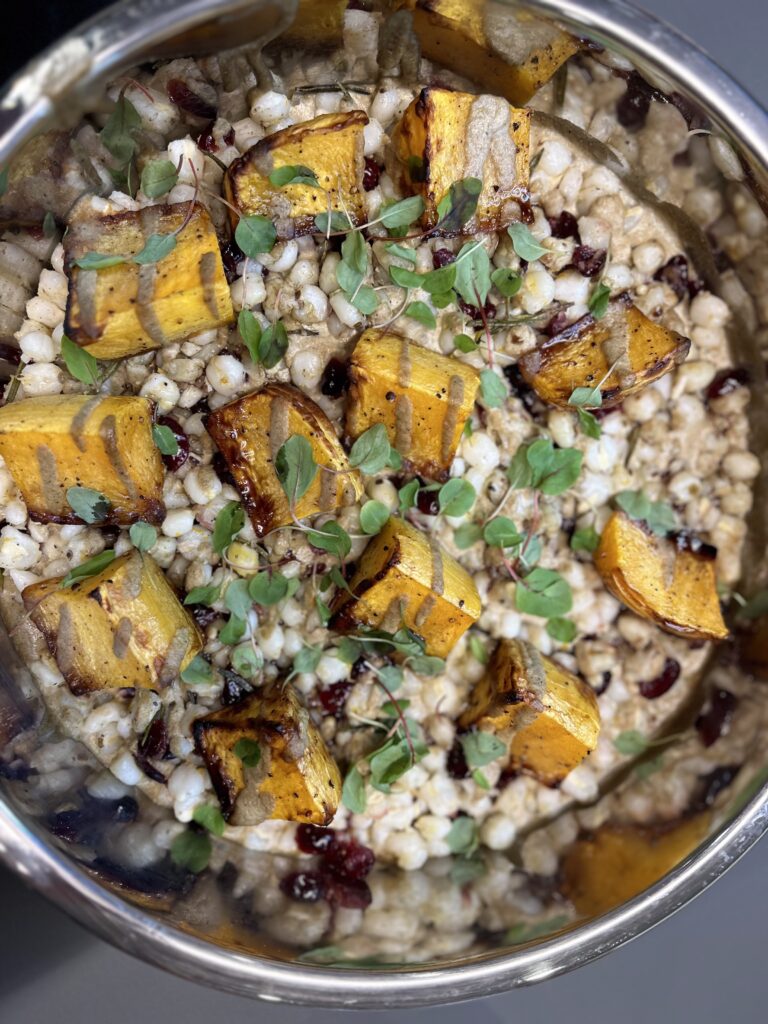 Overhead look at yellow squash over hominy with kanuchi and springs of herbs in chafing dish. 