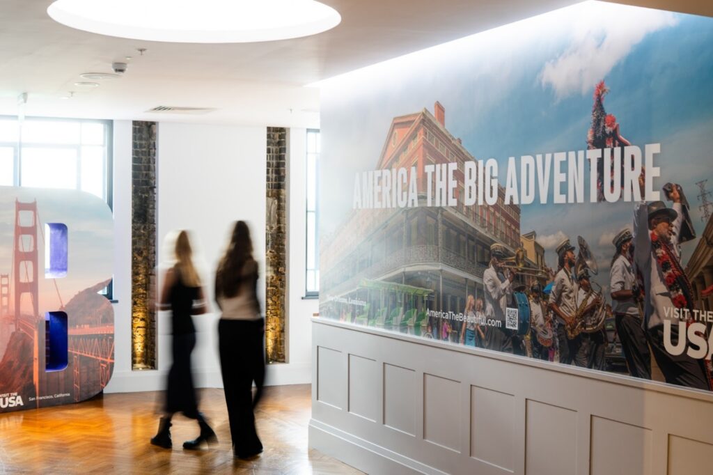 Two blurred people walking down well-lit hallway past sign saying "America the Big Adventure."