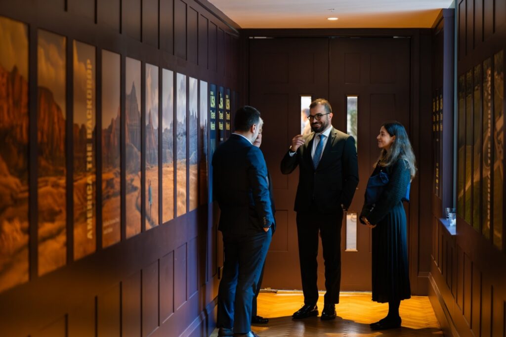 People in suits standing in hallway with dark paneling and images of the American West in etc.venues County Hall. 
