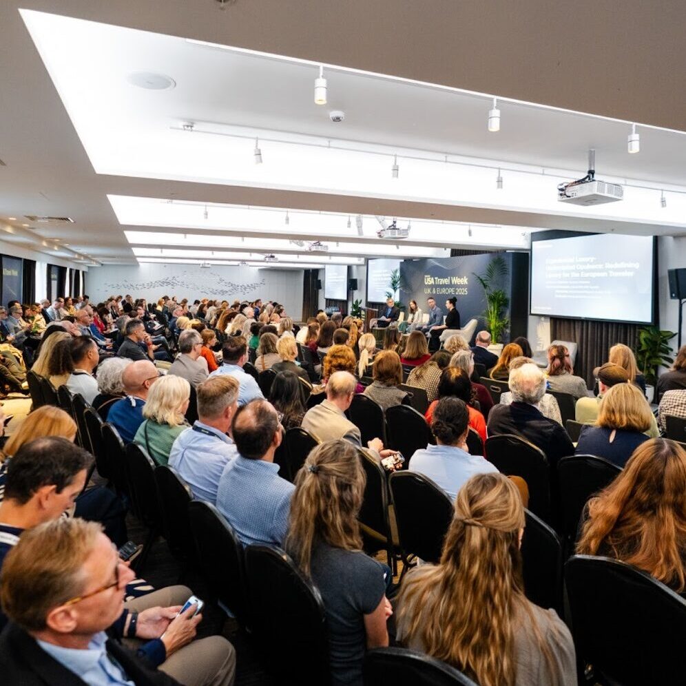 Large conference room in etc.venues County Hall with rows of seats looking at four panelists on stage. 