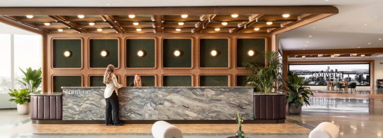 Person greeted at a modern welcome desk at Convene 30 Hudson Yards filled with natural light and two chairs for seating.
